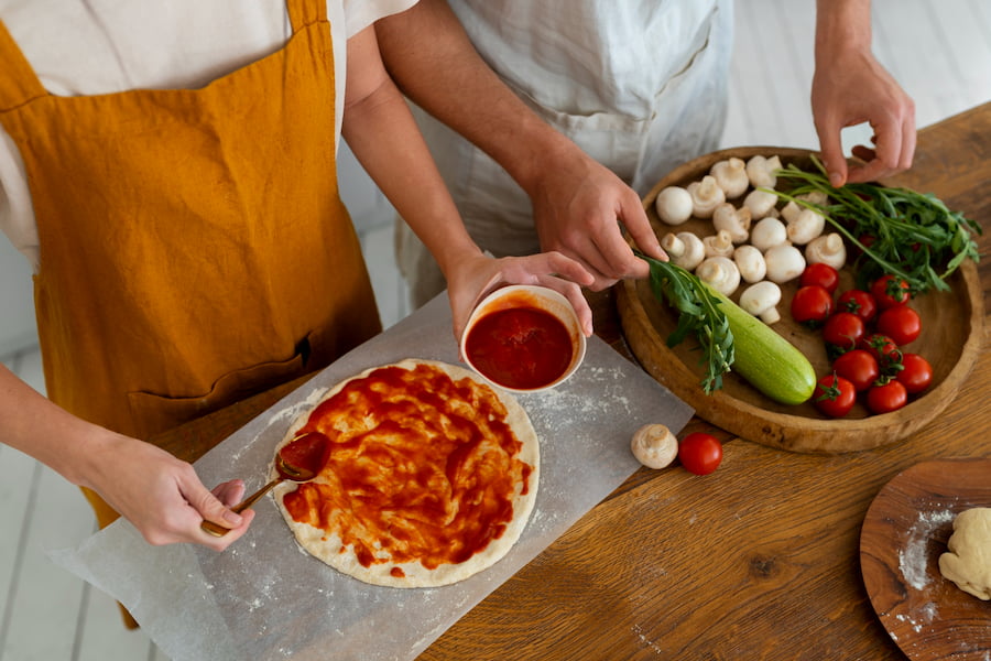 Two individuals making a pizza on a table - part of the process of creating 6 Nutrient-Rich Pizza Sauces from Scratch.